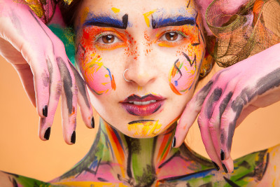 Beautiful fashion woman with bright color face art and body art. Paint on face. Posing in studio. Cr